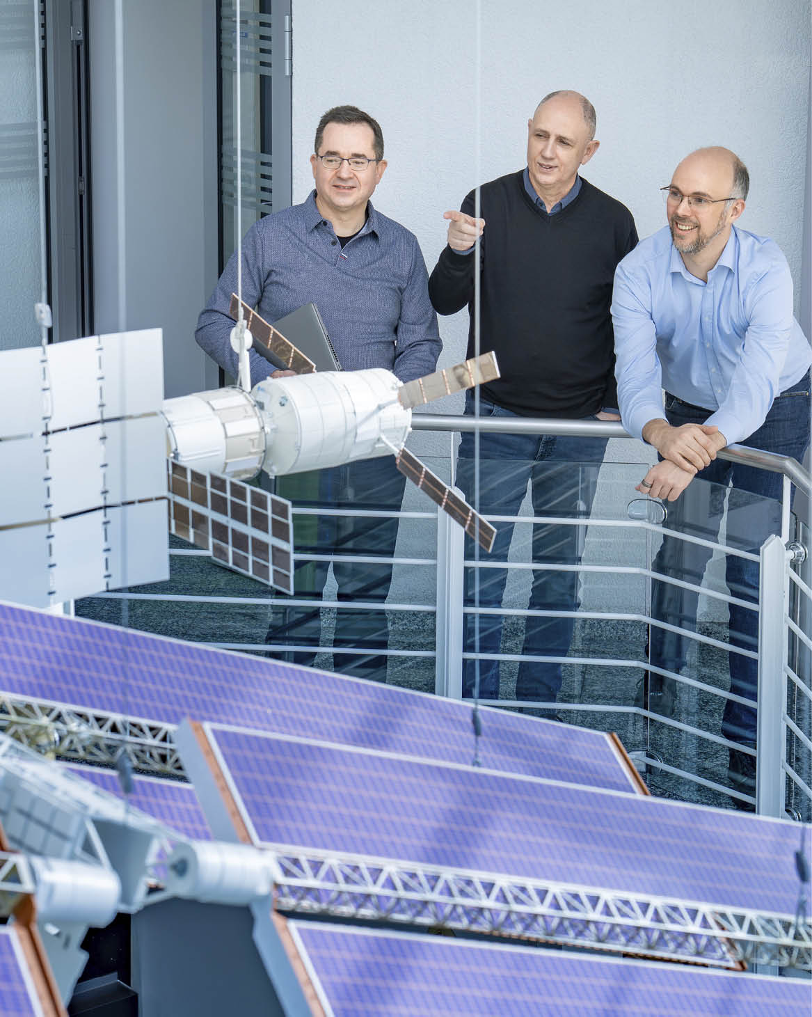 A group of men standing on a glass balcony looking at a solar panel. Description generated by AI